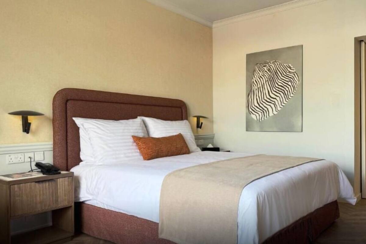 Ein Hotelzimmer mit einem Bett, Nachttischen, einem Wandbild und einer Tür.