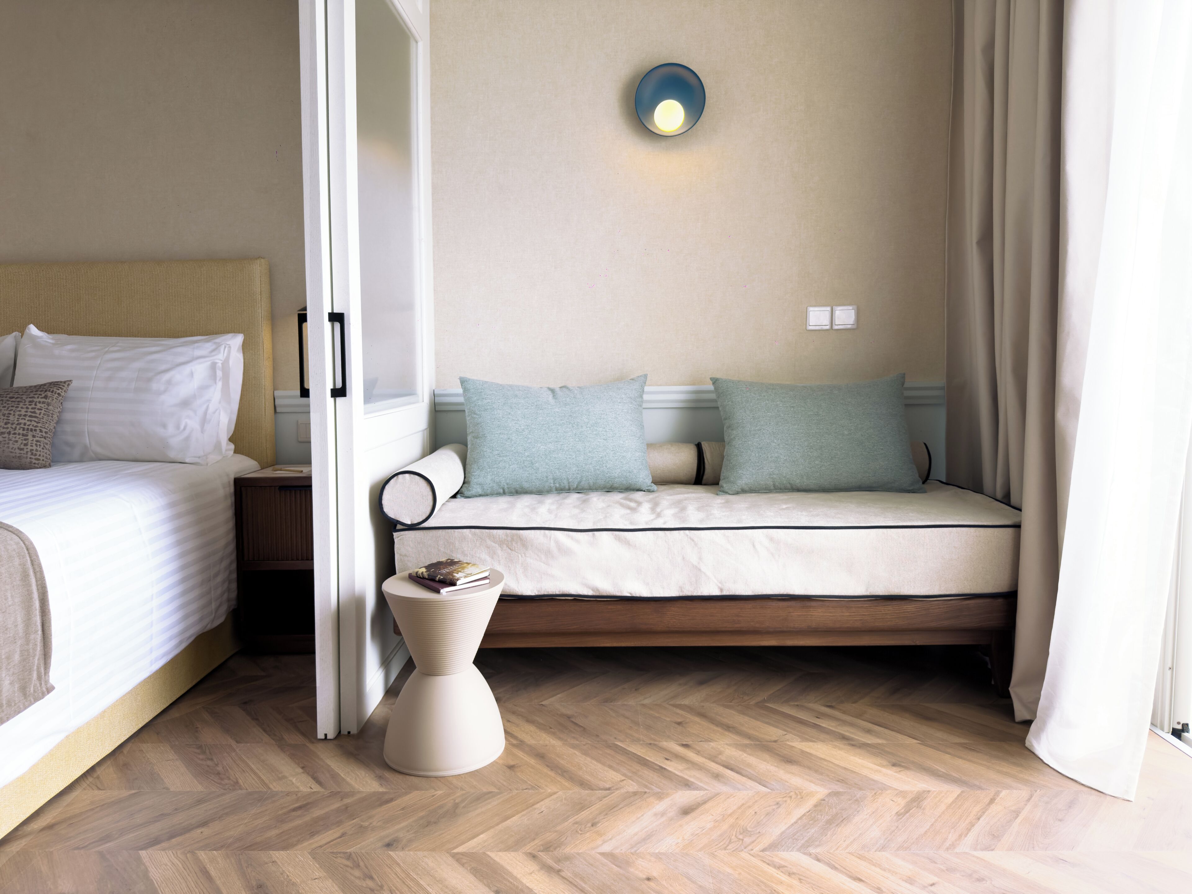 A hotel room with a bed, a sofa, a small table, and a wall-mounted light fixture.