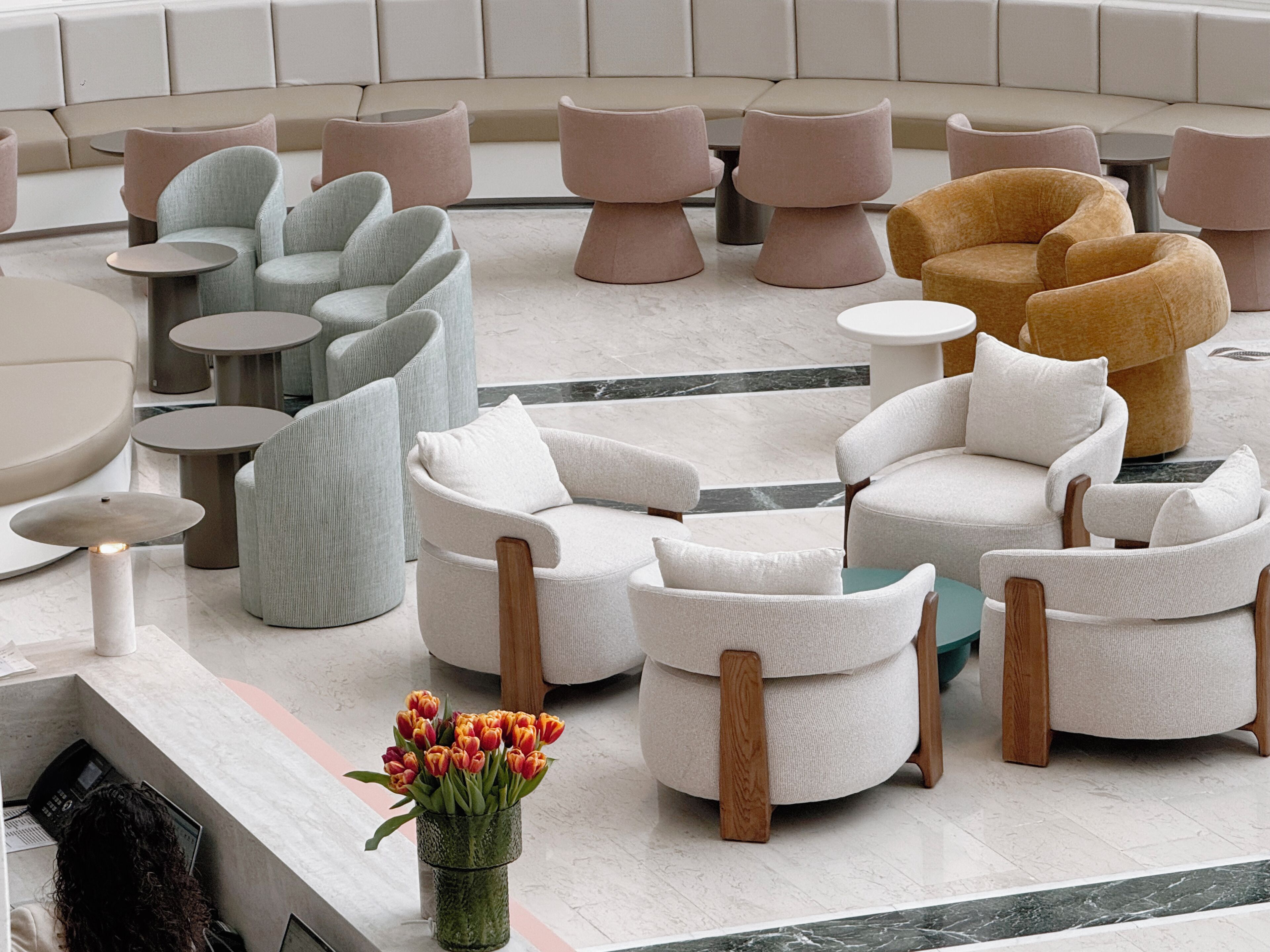 Un área de descanso moderna con diversas opciones de asientos, incluyendo sofás y sillones, suelo de mármol y una mesita con un jarrón de flores.