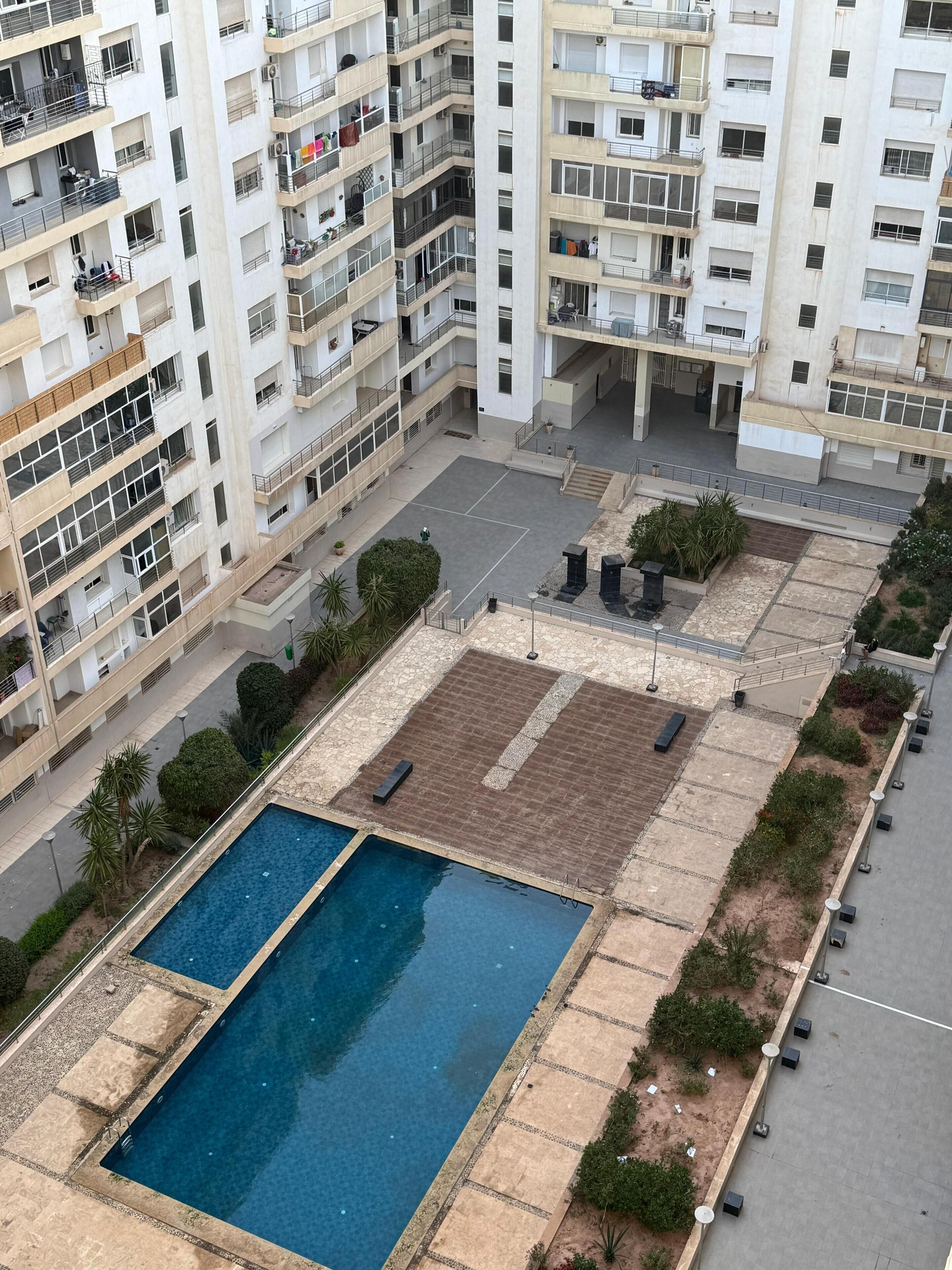 Ein Hochhaus mit mehreren Balkonen, einem Pool auf dem Dach und umliegendem Grün.