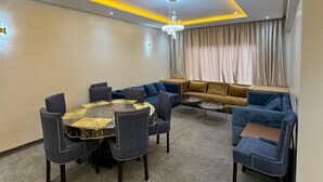 A modern living room with a round table, blue sofas, and a large window with curtains. - Sweat home Pool (Agadir)