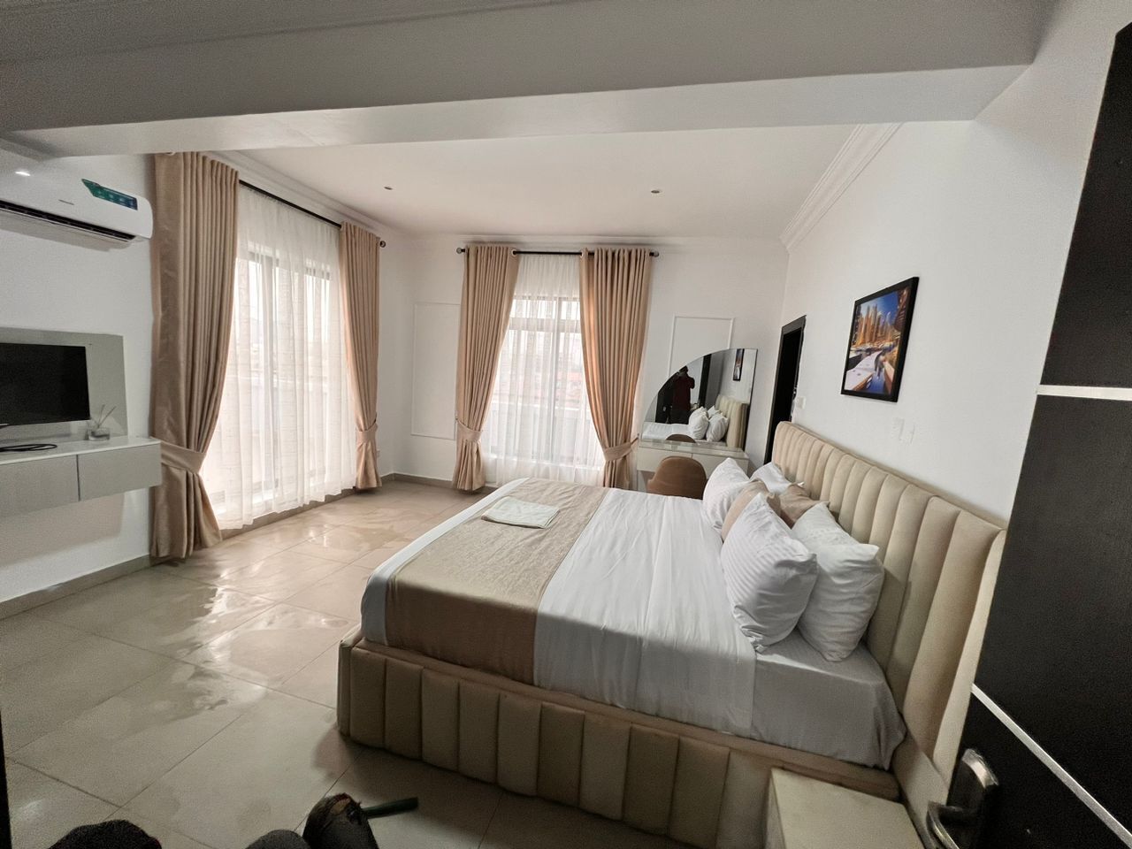 Ein modernes Hotelzimmer mit einem großen Bett, einem Flachbildfernseher, einem Schreibtisch und einem Fenster mit Vorhängen.