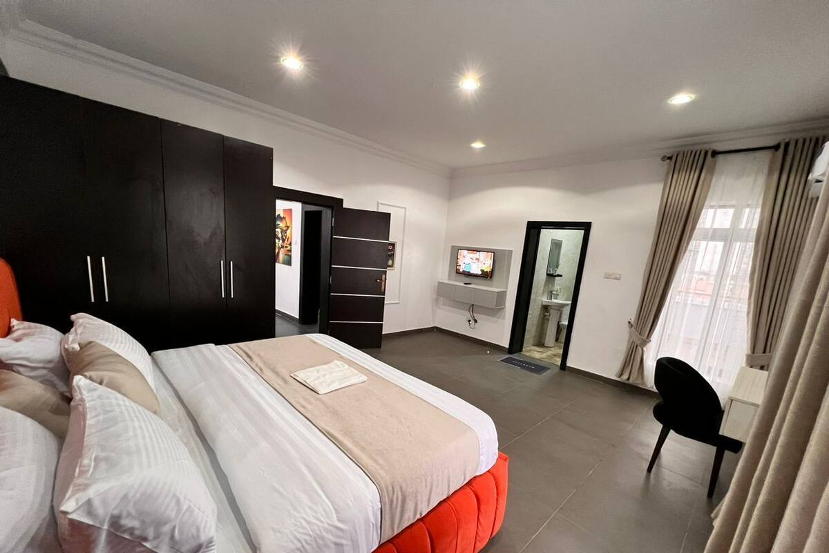 A modern hotel room with a large bed, a wardrobe, a television, and a bathroom visible through an open door.