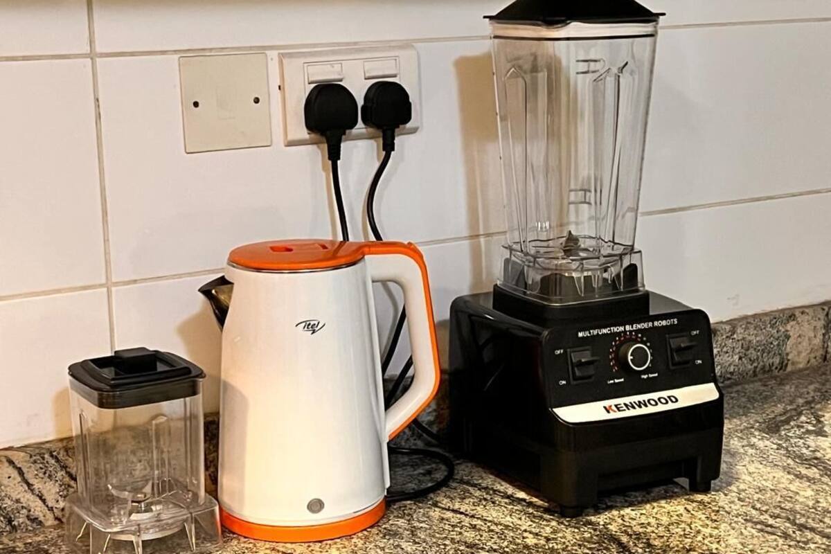 A kitchen with a white and orange coffee maker, a black and orange blender, and a clear blender pitcher.
