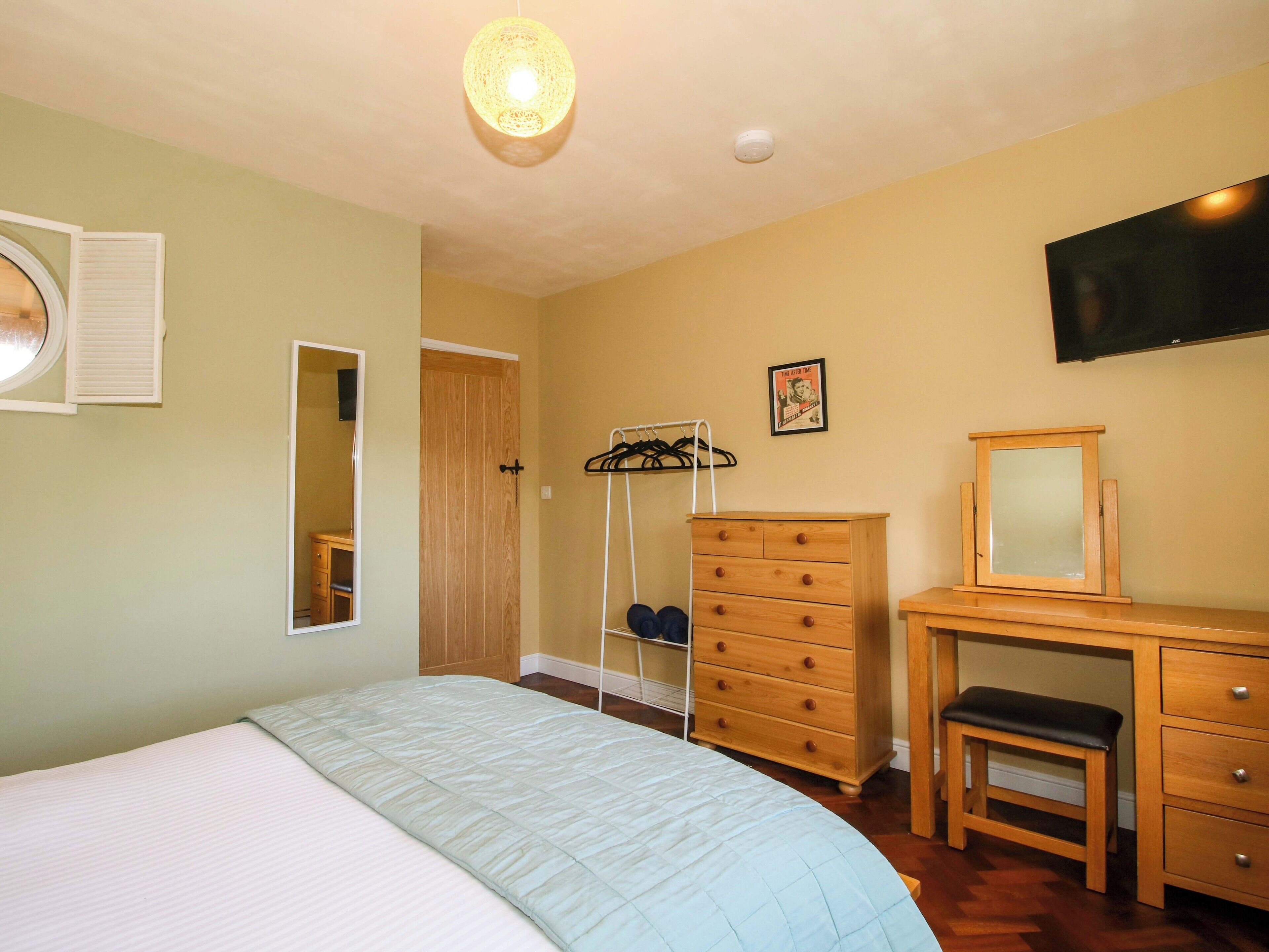 Une chambre à coucher avec un lit, une commode, un miroir et un téléviseur fixé au mur.