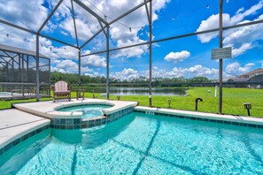 A swimming pool with a hot tub, surrounded by a covered area with chairs, under a clear sky. - Spacious 7BR resort home w/ pool & spa (Kissimmee)