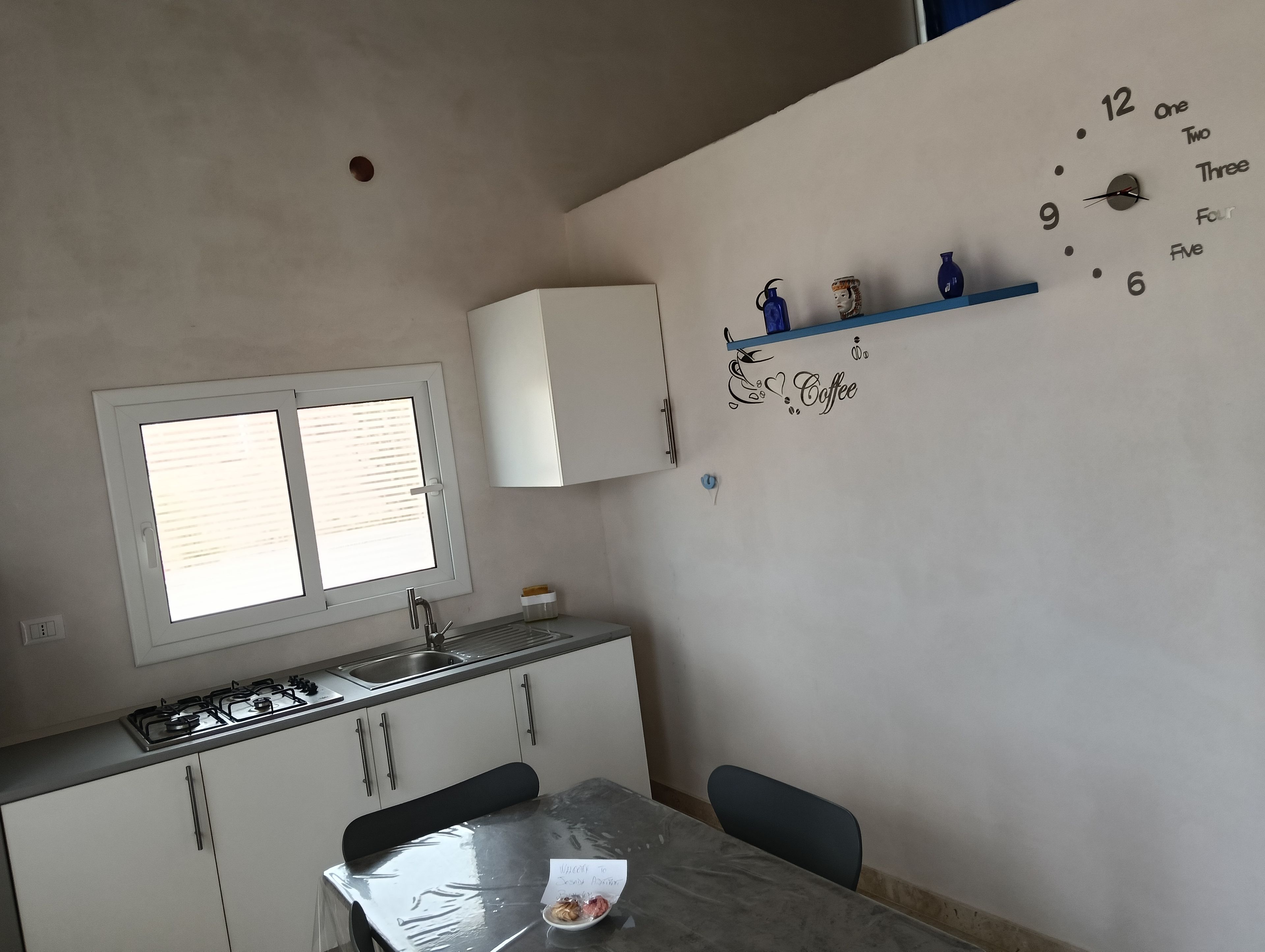 Una cucina con una finestra, un lavello, pensili, un fornello e una sveglia a muro.