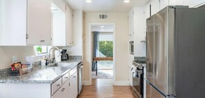 A modern kitchen with white cabinets, a stainless steel refrigerator, and a granite countertop. - Family, Pet & Long Vacation Friendly, Fenced Yard (Sacramento)