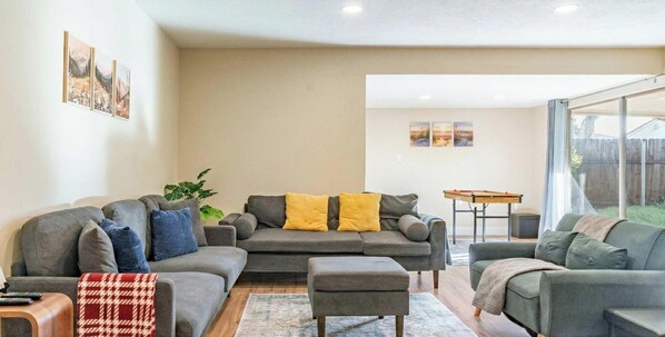 A living room with a grey sofa set, a coffee table, and a small table with a board game. - Family, Pet & Long Vacation Friendly, Fenced Yard (Sacramento)