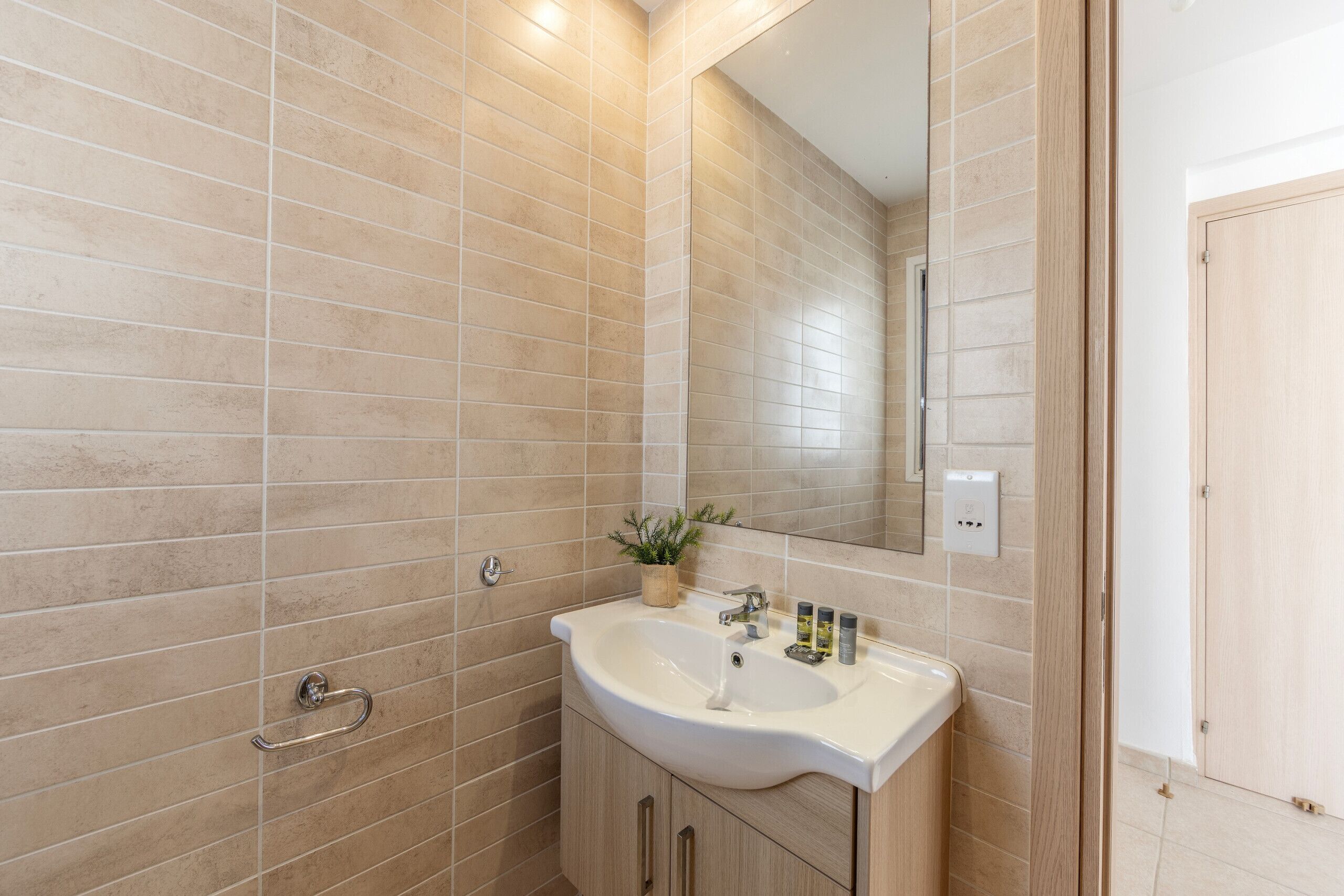 A bathroom with beige tiles, a white sink, a mirror, and a wooden door.