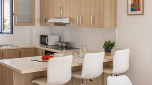 A modern kitchen with wooden cabinets, a microwave, a stove, and a small island with white chairs. - Protaras Seaside Villa Protamare 32 (Paralimni)