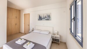 A bedroom with a bed, nightstands, a wooden wardrobe, a painting, and a window. - Protaras Seaside Villa Protamare 32 (Paralimni)