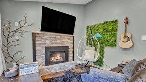 A living room with a stone fireplace, a hanging chair, a guitar wall, and a television. - King Size - Romantic - Massage - Pet Friendly (Blakeslee)