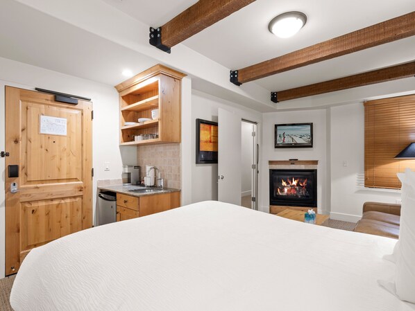 Un dormitorio con una cama grande, chimenea, vigas de madera, una zona de cocina y una puerta con un cartel.