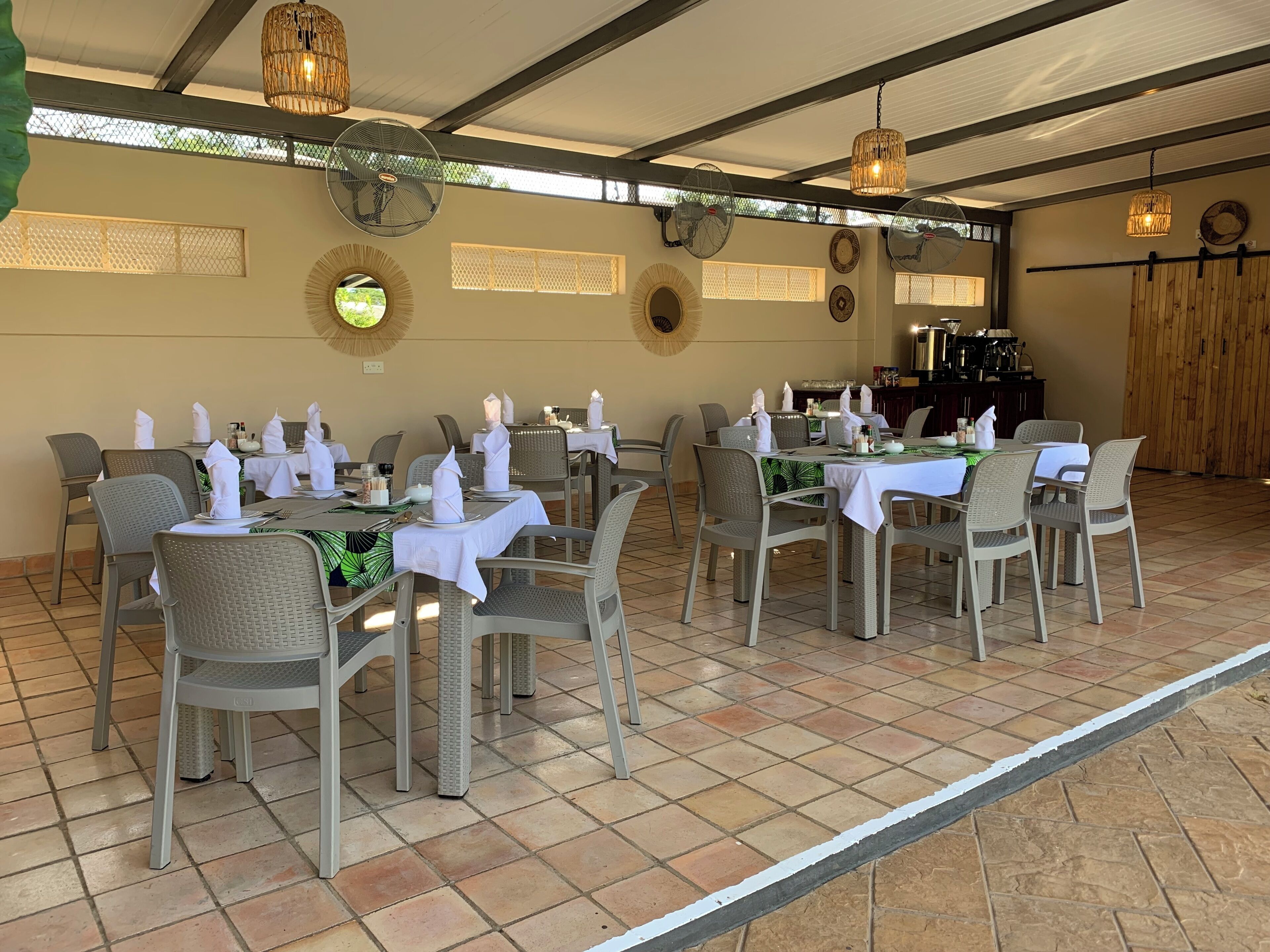 Een restaurant met meerdere eettafels, rieten stoelen en plafondventilatoren.