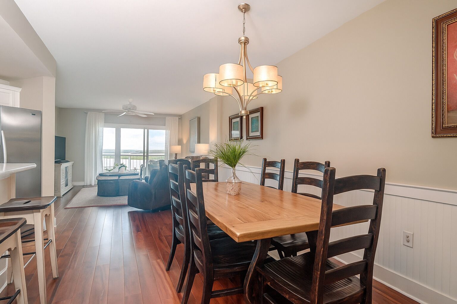 A dining area with a wooden table, dark chairs, a chandelier, and a view to the outside.