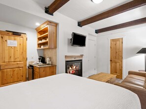 Una habitación acogedora con cama, chimenea, armarios de madera, televisor y una pequeña mesa.