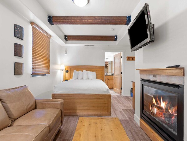 Un dormitorio acogedor con cama, televisor, chimenea y un banco de madera.