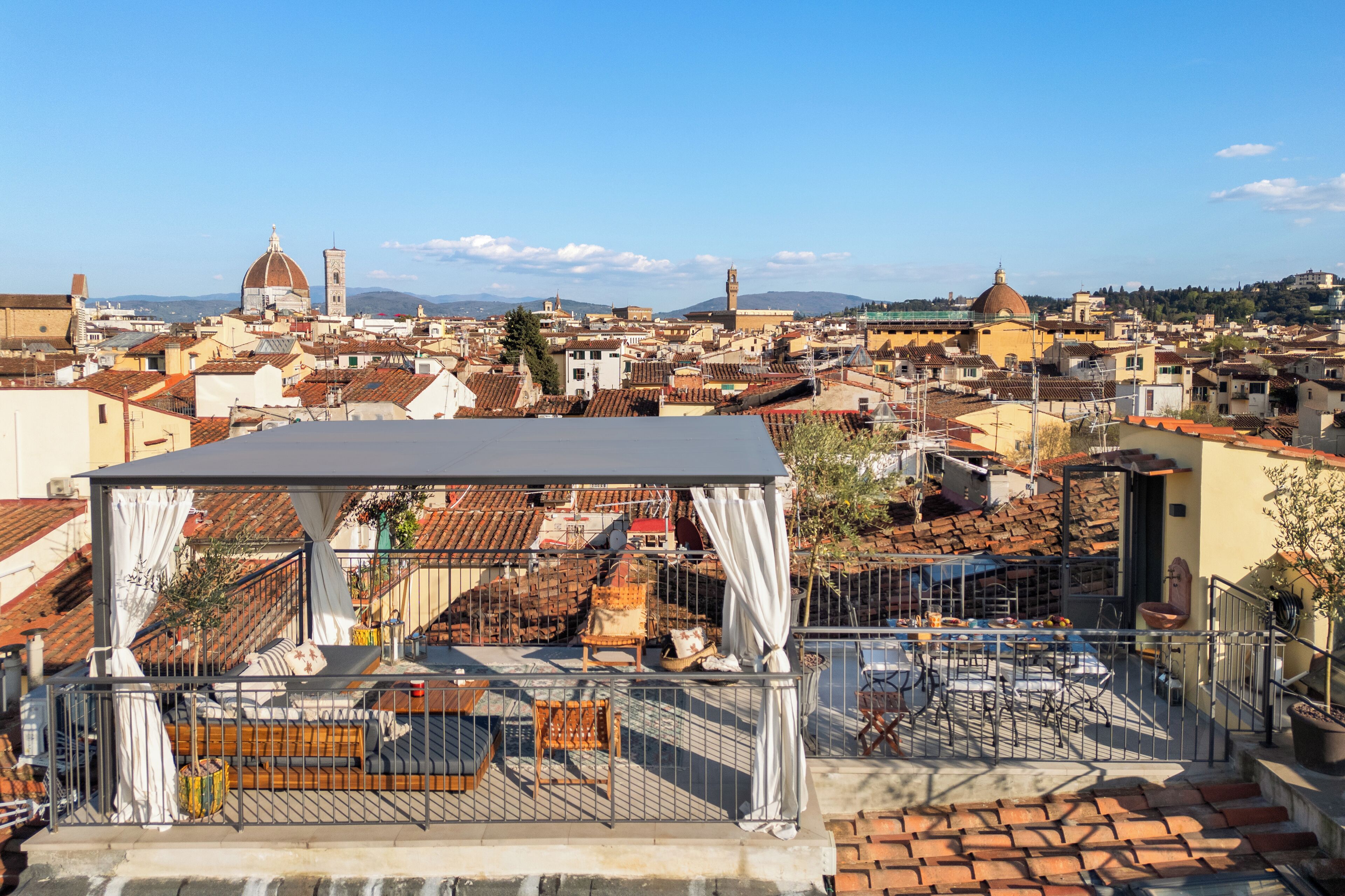 A rooftop terrace with a covered seating area, a view of the cityscape, and a clear sky.