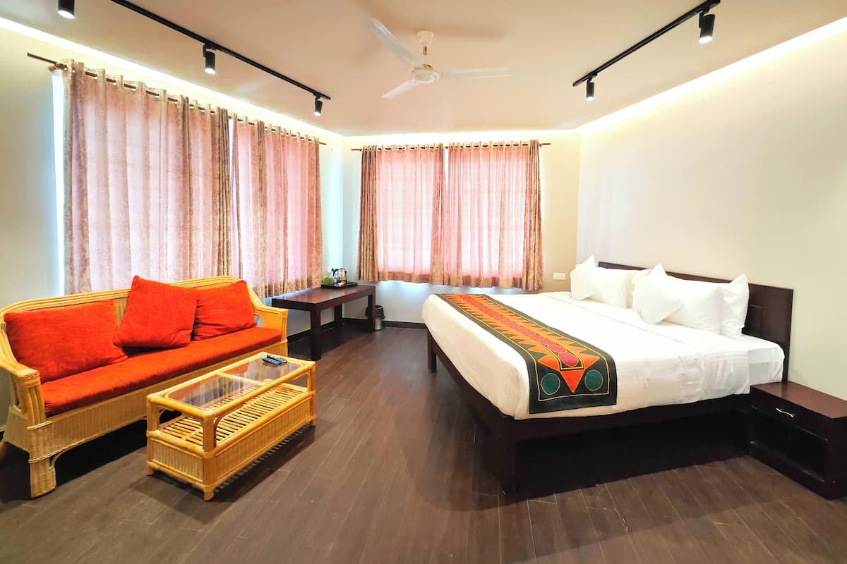 A hotel room with a bed, a sofa, a coffee table, a desk, and curtains.