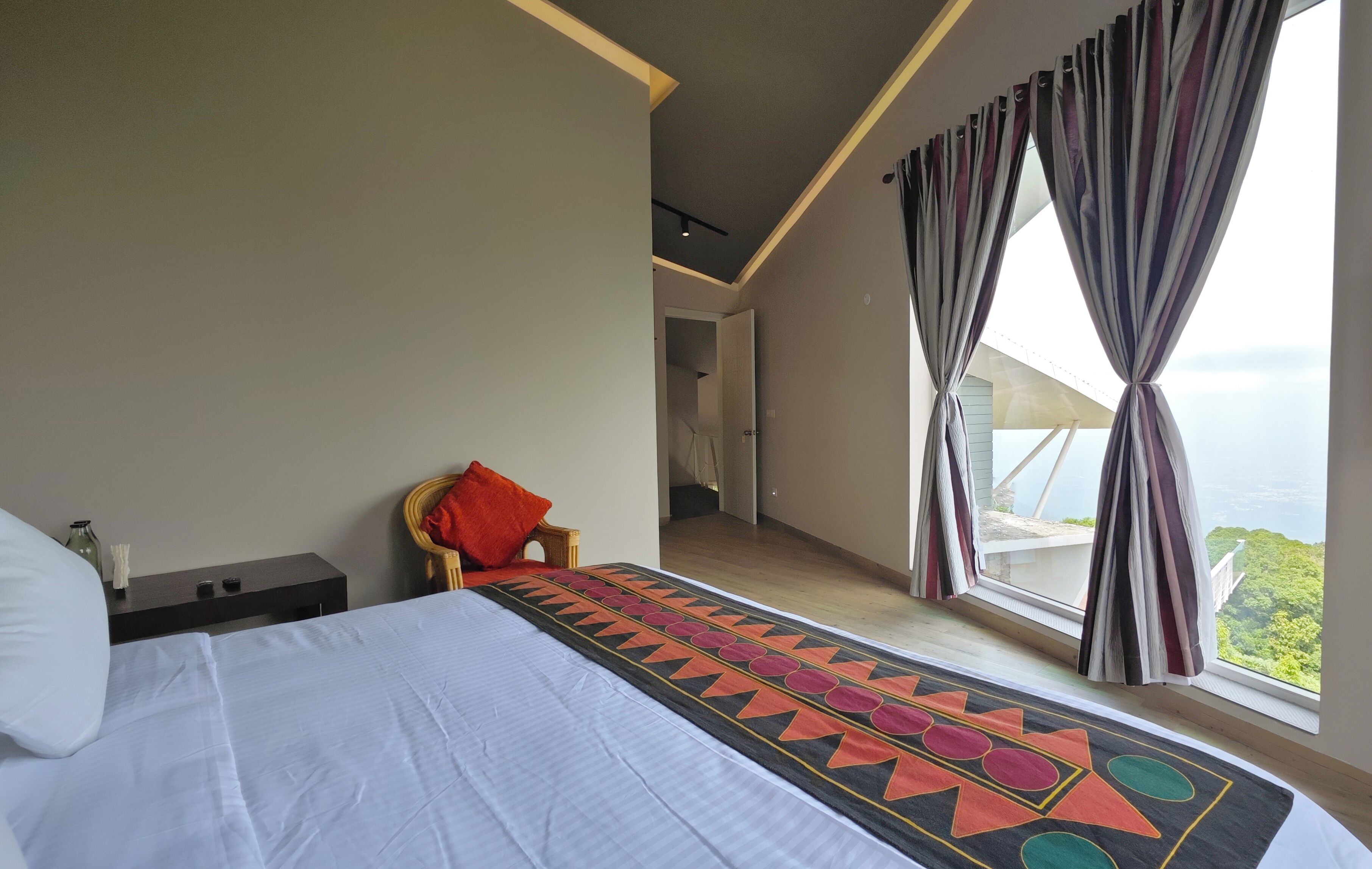 Un dormitorio con una cama grande, una mesita de noche, una silla y vistas al exterior.