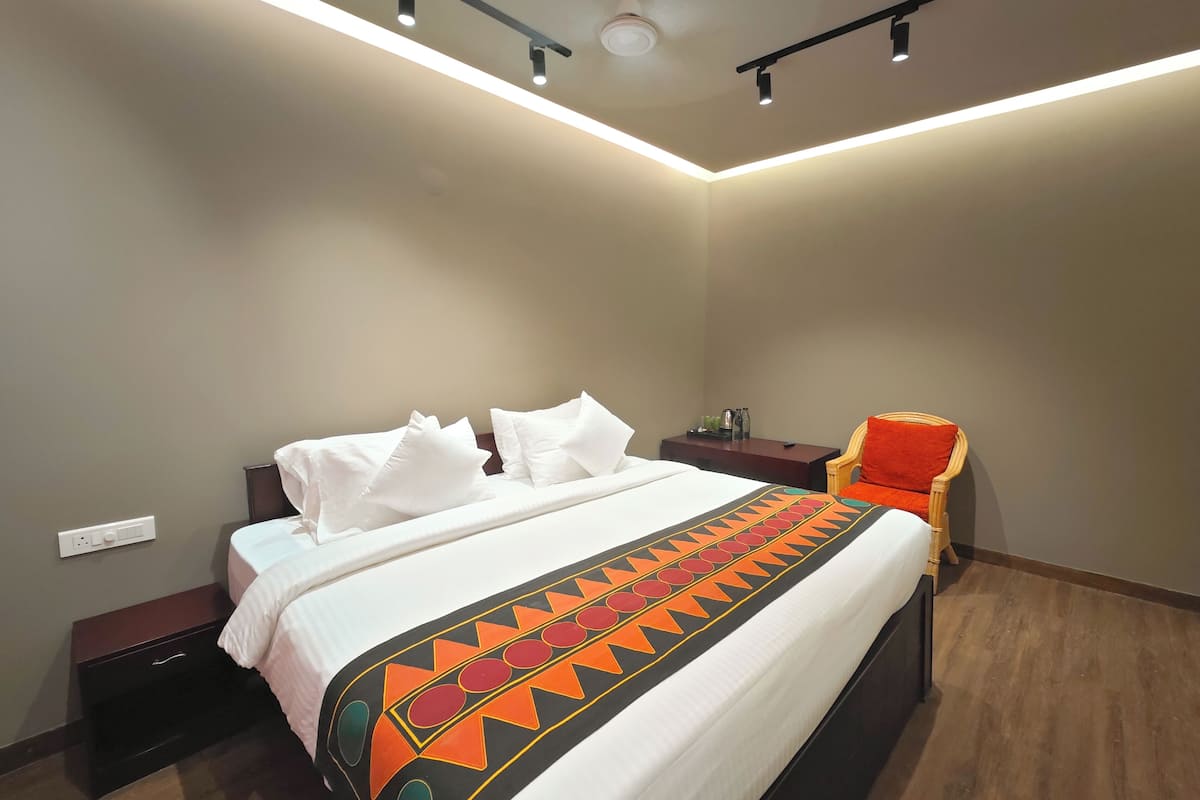 A modern hotel room with a neatly made bed, a nightstand, a chair, and a ceiling light fixture.