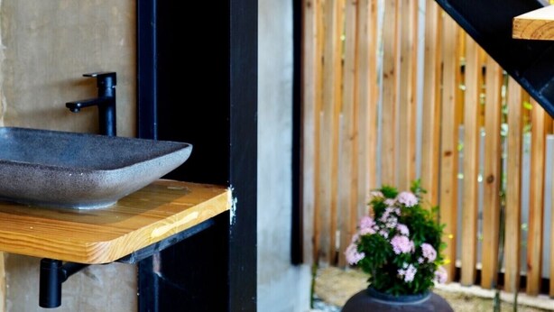 A modern bathroom with a stone sink, wooden shelves, a black metal staircase, and a potted plant. - Mayfair Garden Resort (Panglao)