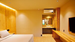 A modern hotel room with a wooden headboard, a large bed, a wooden bench, a TV, and a bathroom visible through an open door. - Mayfair Garden Resort (Panglao)