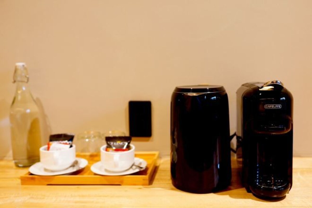 A wooden tray with two white cups and a bottle, accompanied by two black coffee makers.