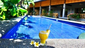 A swimming pool with a drink on the edge, surrounded by greenery and a building with a tiled roof. - Mayfair Garden Resort (Panglao)