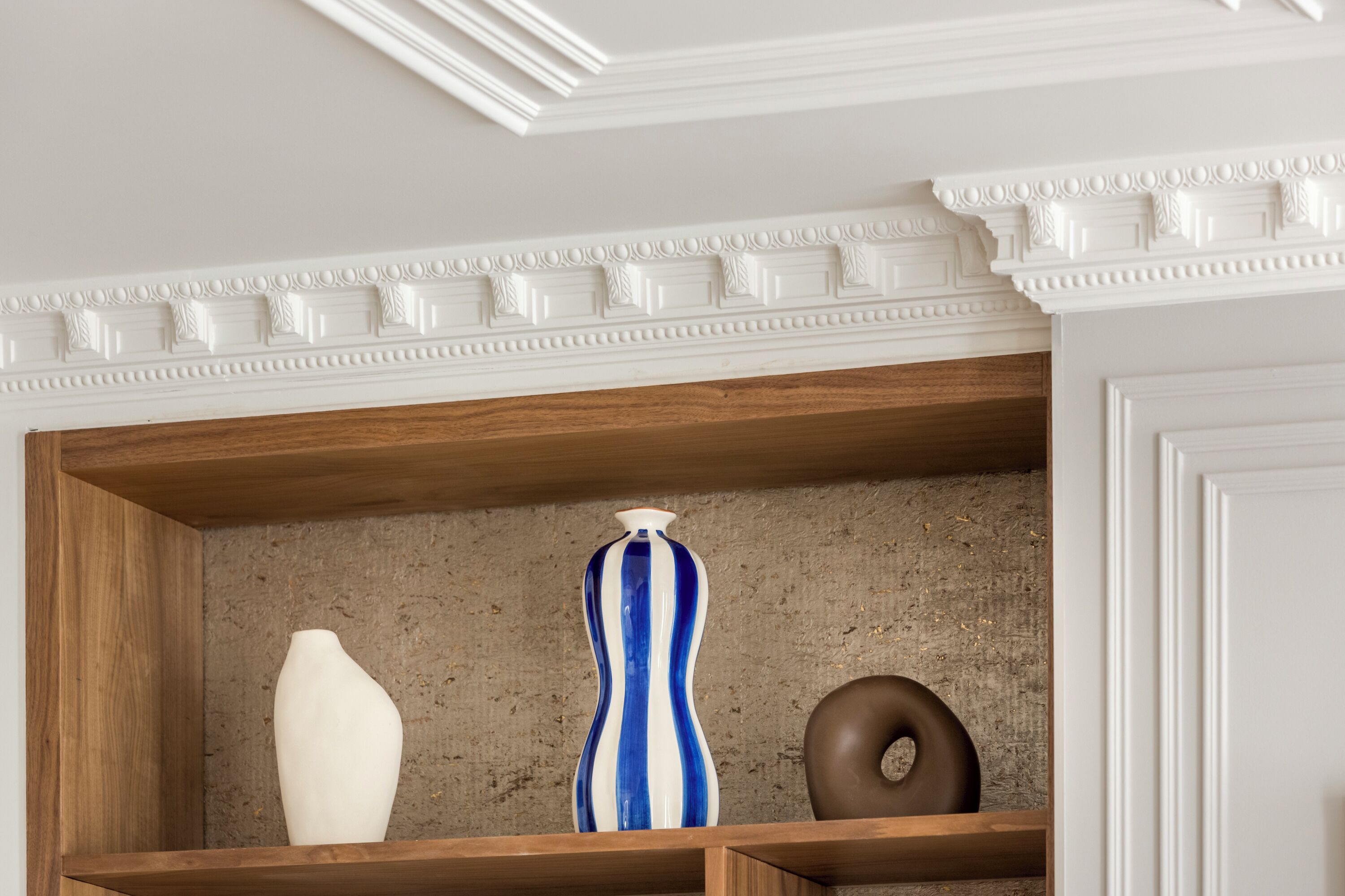 A shelf with three vases: a white vase, a blue and white striped vase, and a brown vase.