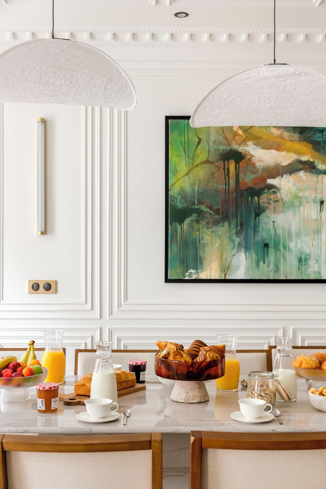 A dining area with a white table set for breakfast, including fruits, pastries, and beverages.