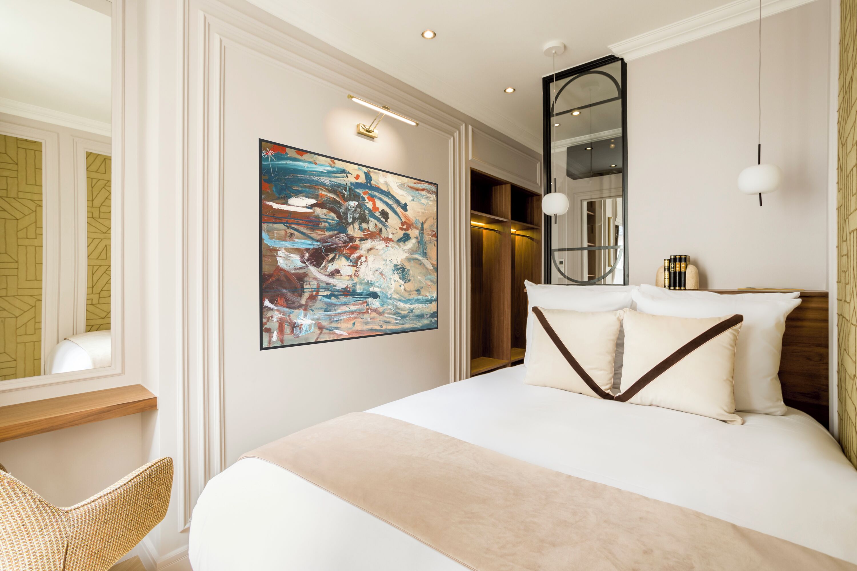 A modern hotel room with a large bed, a painting, a mirror, and a wooden side table.
