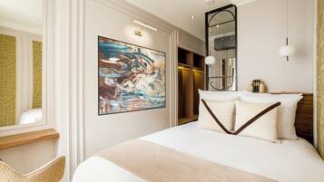A modern hotel room with a large bed, a painting, a mirror, and a wooden side table.