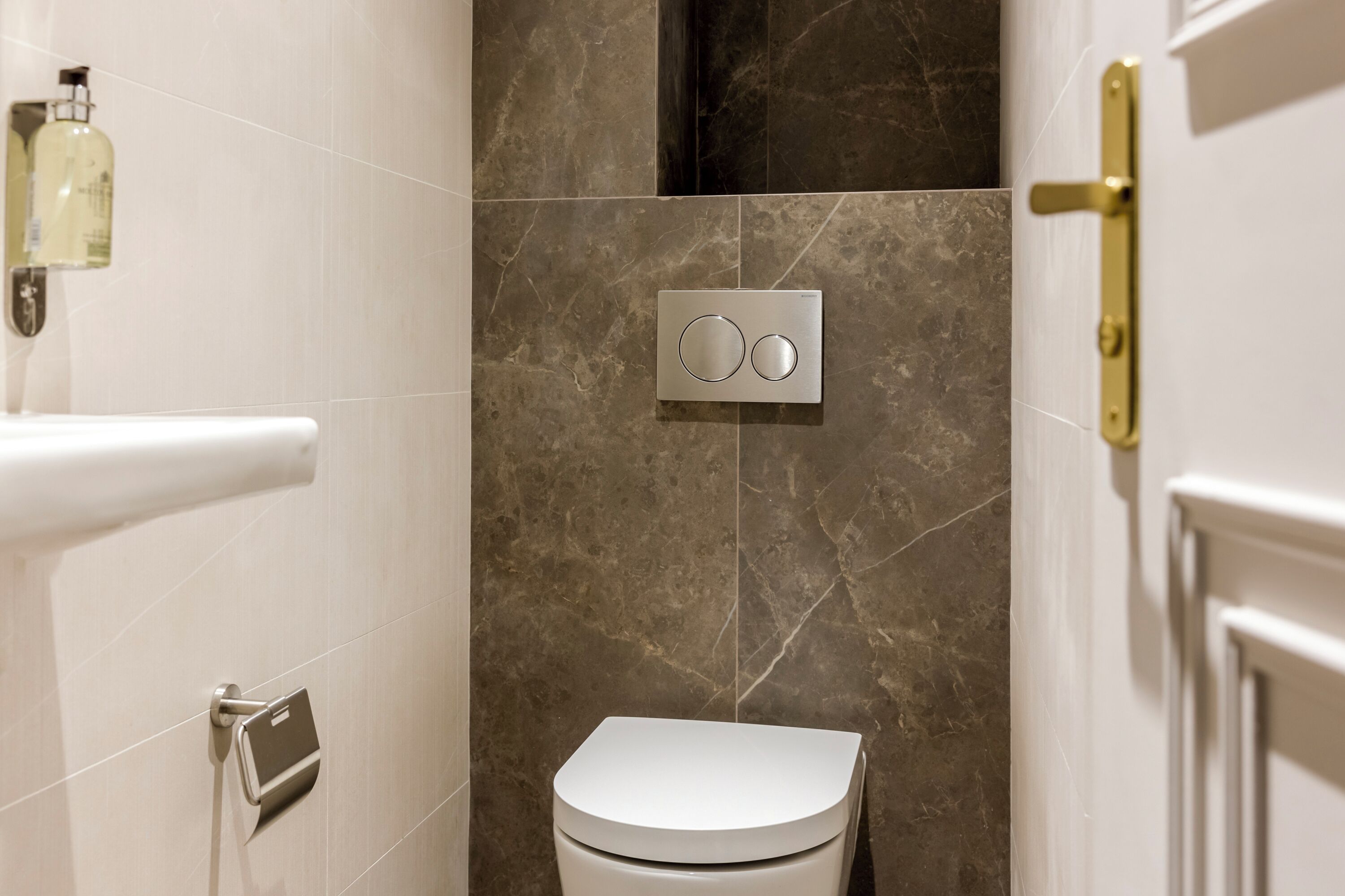 A modern bathroom with a white toilet, a wall-mounted control panel, and a marble-tiled shower area.