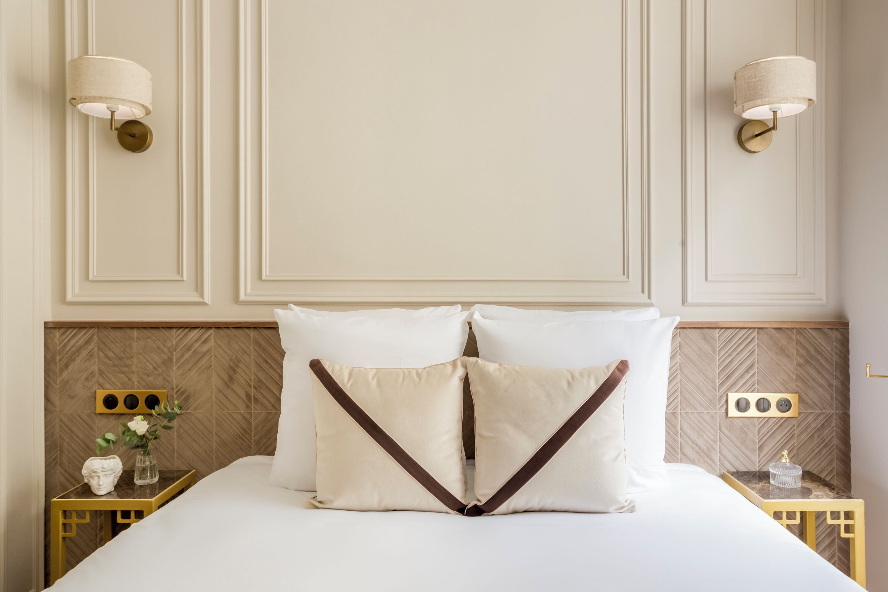 A neatly made bed with two pillows, a bedside table with a vase and a decorative item, and wall-mounted lamps.