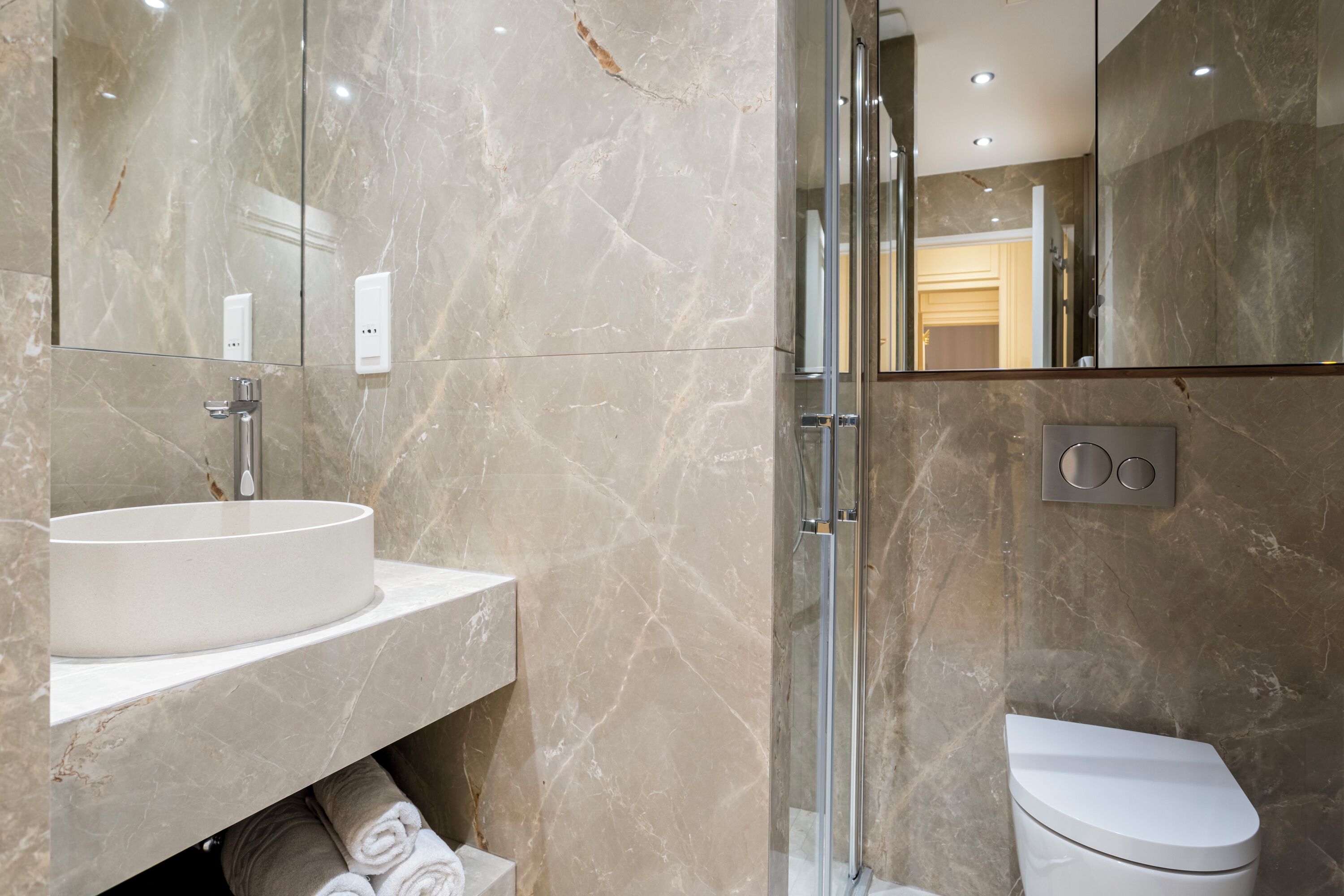 A modern bathroom with a marble sink, a glass shower enclosure, and a toilet.