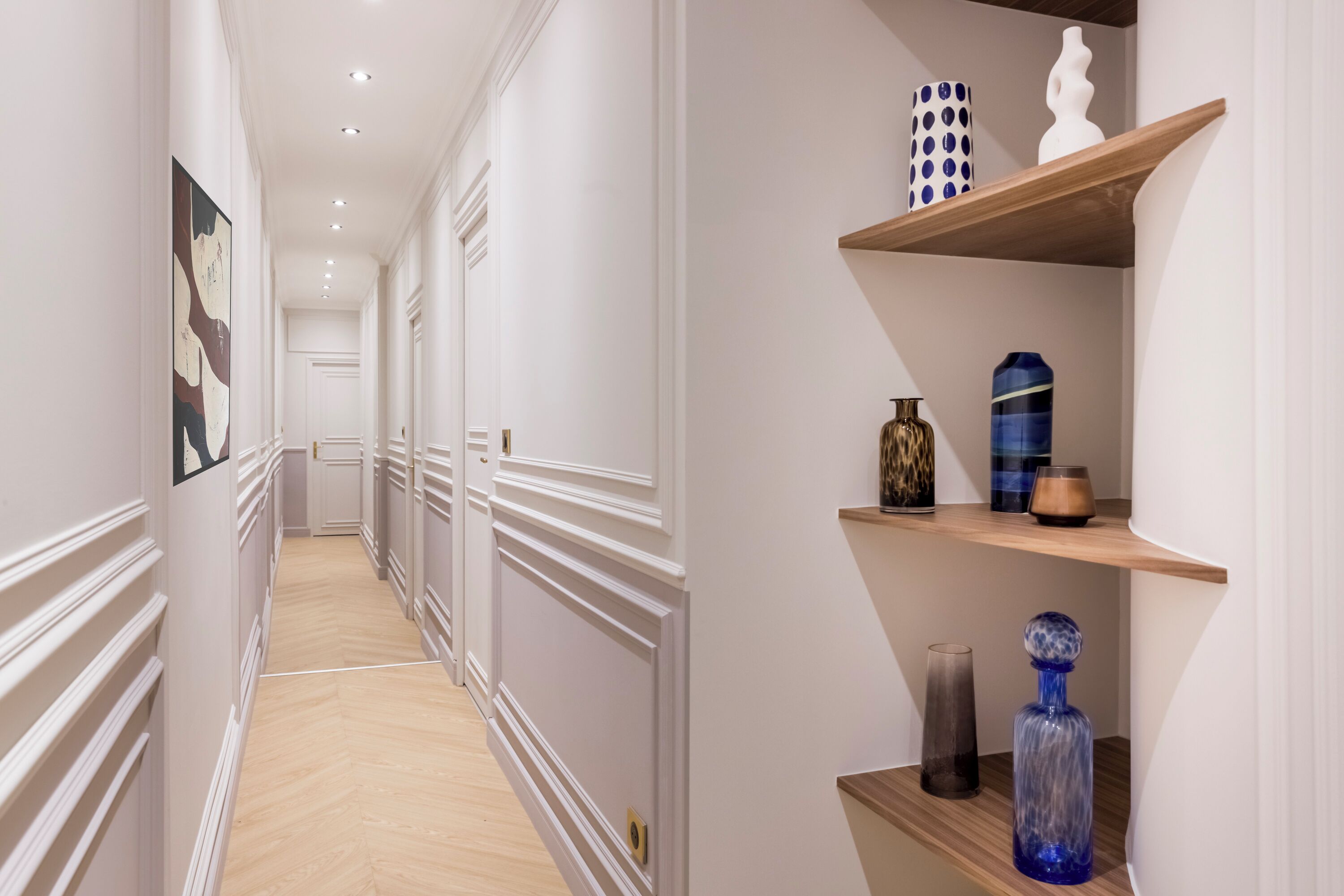 A hallway with white walls, wooden floors, and decorative shelves with vases and sculptures.