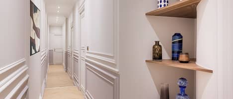 A hallway with white walls, wooden floors, and decorative shelves with vases and sculptures.