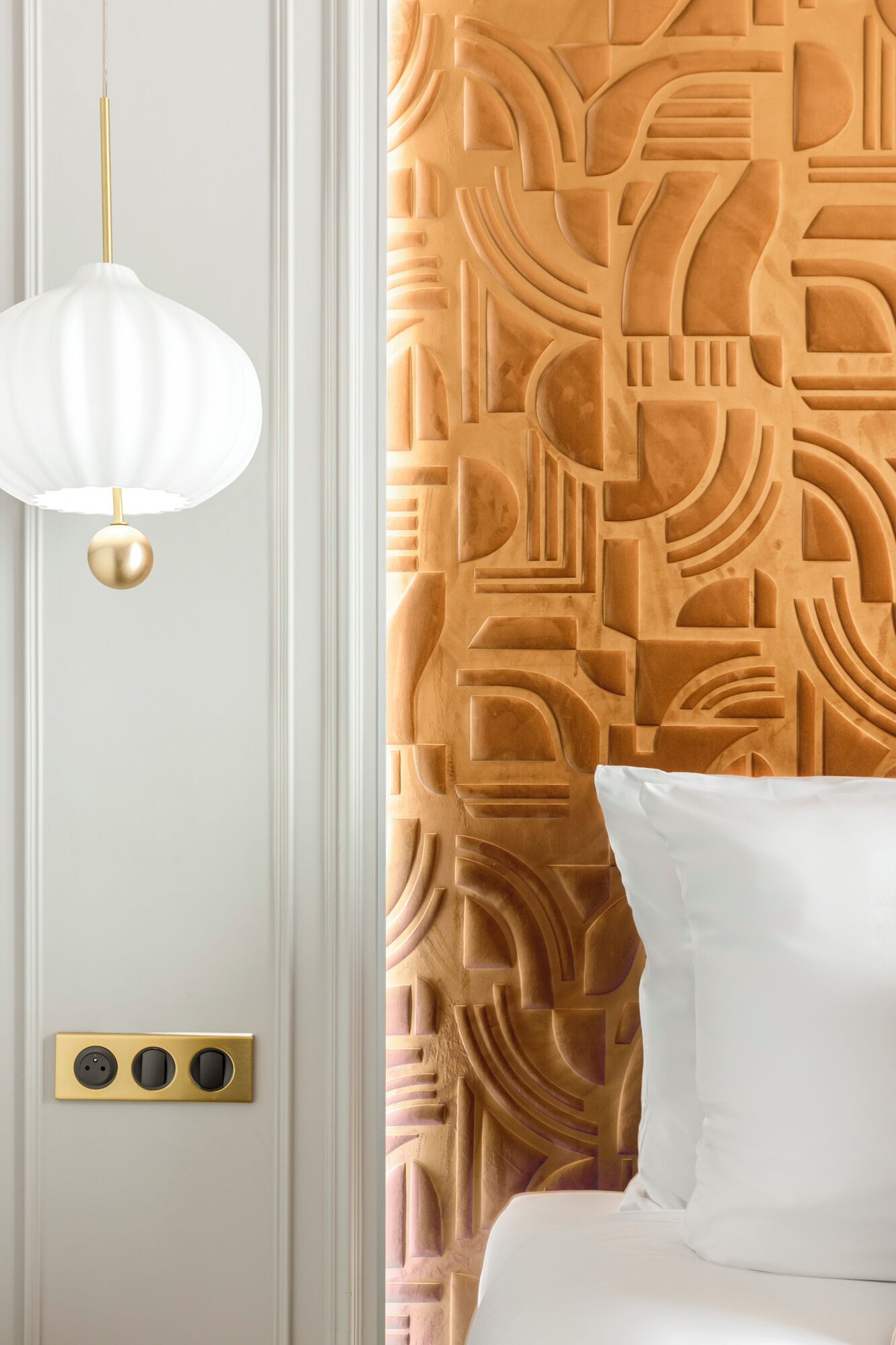 A room with a white wall, a textured orange wall, a white pillow, and a hanging light fixture.
