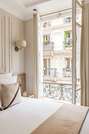 Een hotelkamer met een bed, een nachtkastje en uitzicht op een balkon met decoratieve hekwerk en plantenpotten.