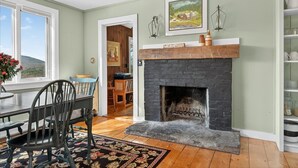 A room with a fireplace, a dining table with chairs, a rug, and a view of the outdoors.