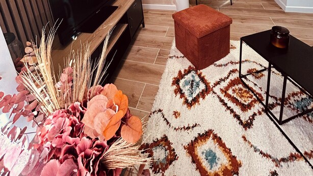 A modern living room with a flat-screen TV, a wooden accent wall, a staircase, and a patterned rug. - Cosy house (Pontarmé)