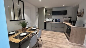 A modern kitchen with a dining area, featuring a wooden table, white chairs, and a built-in oven. - Cosy house (Pontarmé)