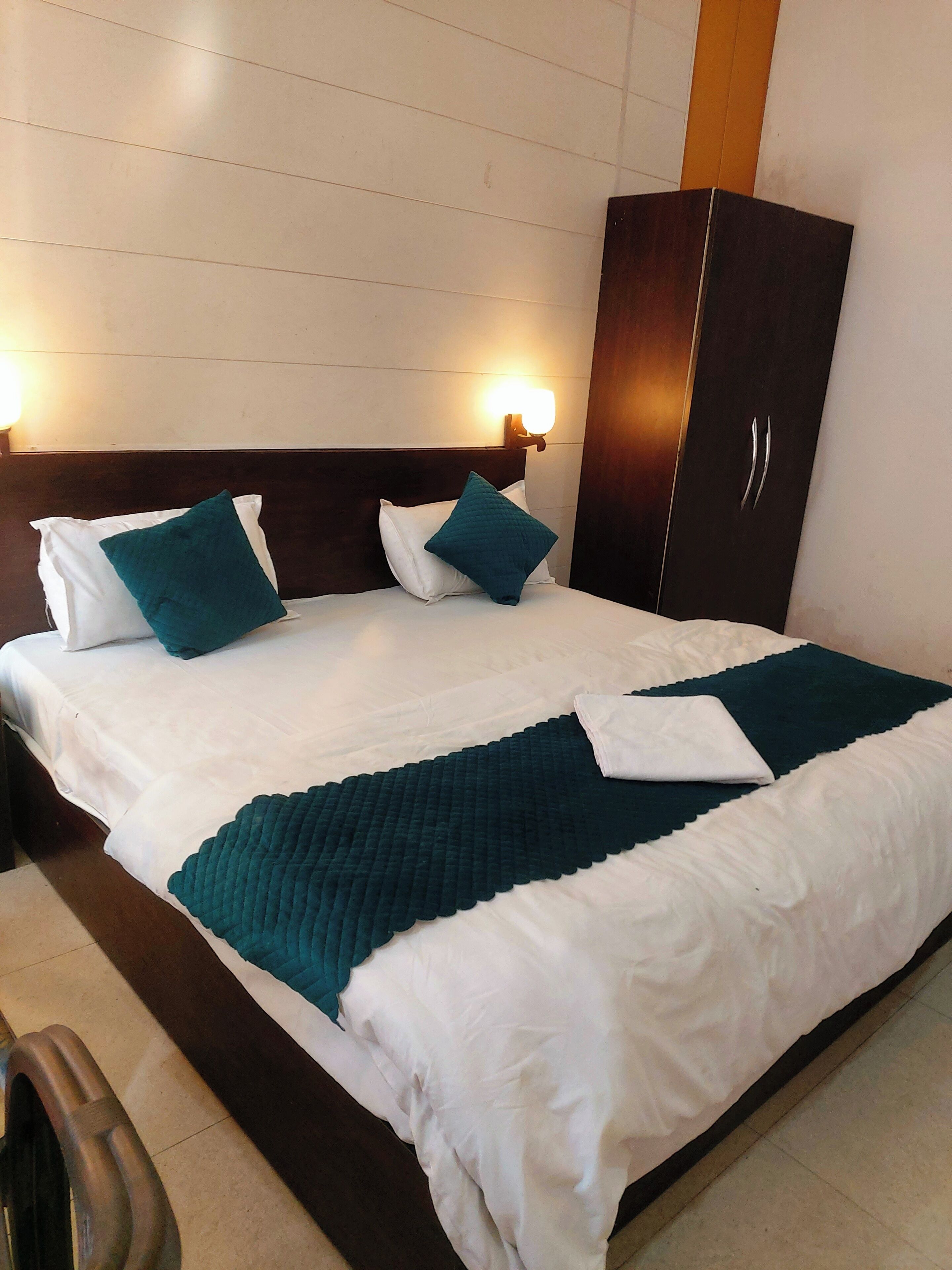 A neatly made bed with white and teal bedding, a dark wooden headboard, and a wall-mounted light fixture.