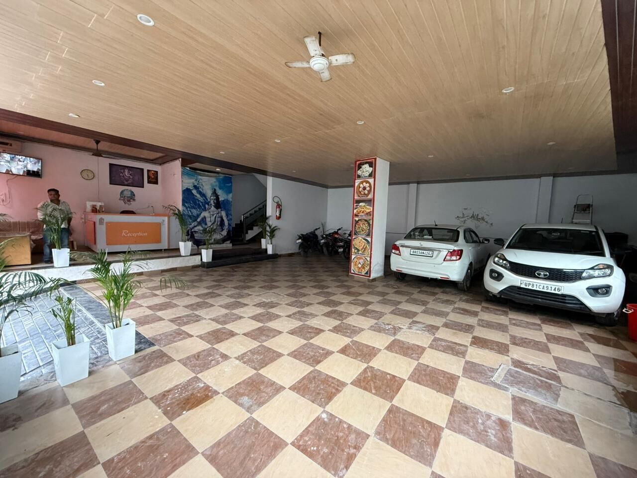 A reception area with a checkered floor, a reception desk, a column with a menu, and two parked cars.