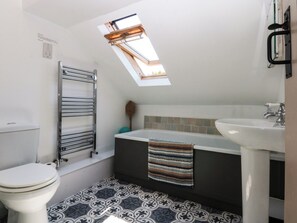 A small bathroom with a skylight, a toilet, a bathtub, and a sink.