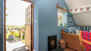 A cozy room with a fireplace, a wicker sofa, and a view of the outdoors. - Borth Arian Boat House (Holyhead)