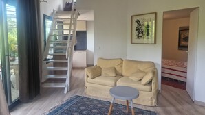 A living room with a sofa, a small round table, a patterned rug, a staircase, and a kitchen area. - ATYPICAL ARCHITECT-DESIGNED HOUSE (Vence)