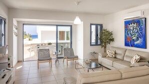 A modern living room with a sofa, chairs, a coffee table, and a painting. - Protaras Seaside Villa Protamare 32 (Paralimni)